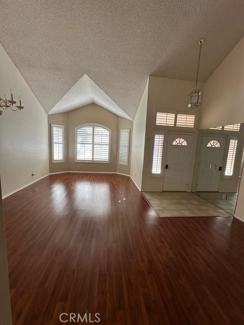 foyer entrance featuring vaulted ceiling, wood-type flooring, a notable chandelier, and a textured ceiling