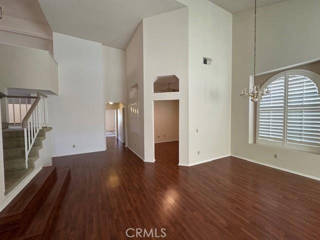 unfurnished living room with a towering ceiling, dark hardwood / wood-style floors, and an inviting chandelier