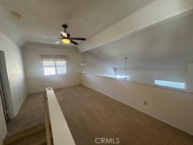 carpeted spare room featuring ceiling fan, lofted ceiling with beams, and a textured ceiling