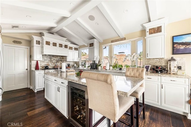 kitchen with beverage cooler, white cabinets, vaulted ceiling with beams, a kitchen breakfast bar, and backsplash