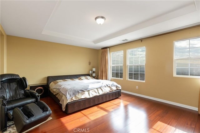 bedroom with a tray ceiling, visible vents, baseboards, and wood finished floors