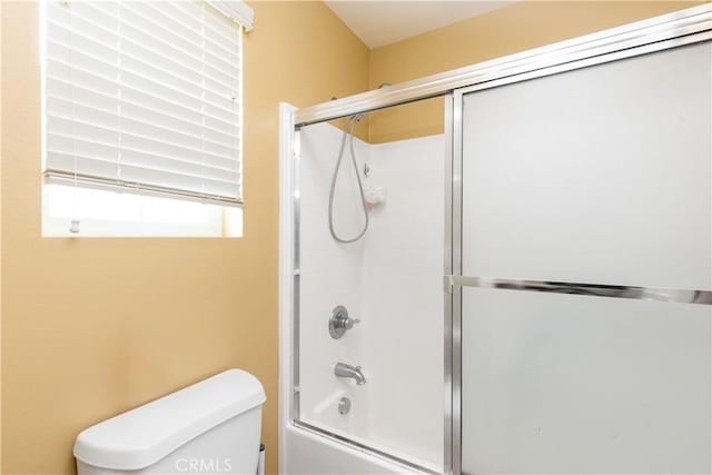 bathroom with toilet and shower / bath combination with glass door