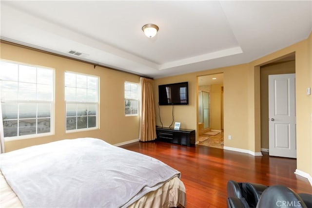 bedroom with dark wood-style flooring, a raised ceiling, visible vents, connected bathroom, and baseboards