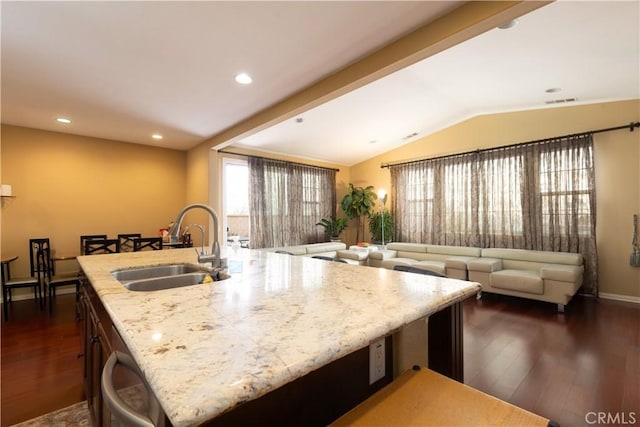 kitchen with dark wood-style floors, vaulted ceiling, a sink, and an island with sink