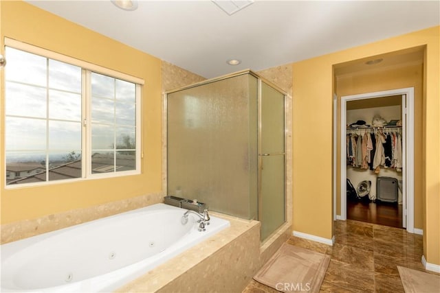 full bathroom featuring a spacious closet, a jetted tub, a shower stall, and baseboards