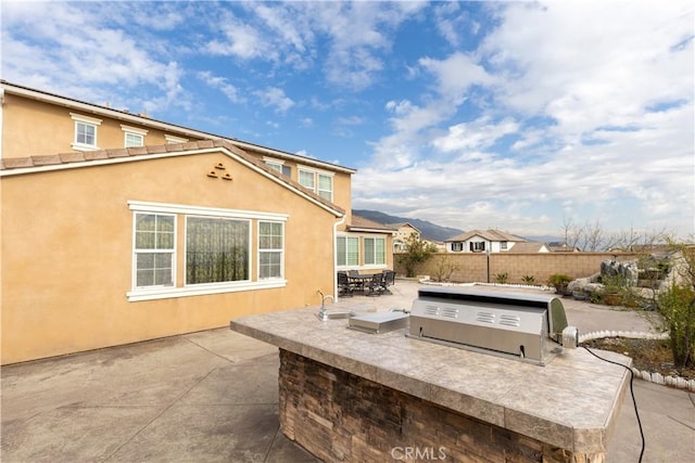 view of patio / terrace featuring outdoor dining area, a mountain view, a sink, fence, and exterior kitchen