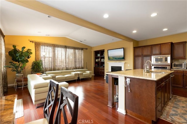 kitchen with a kitchen island with sink, stainless steel appliances, a sink, open floor plan, and vaulted ceiling