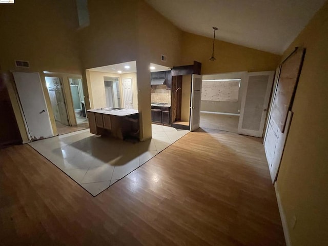 kitchen with a kitchen island, dark brown cabinetry, light wood-type flooring, and high vaulted ceiling