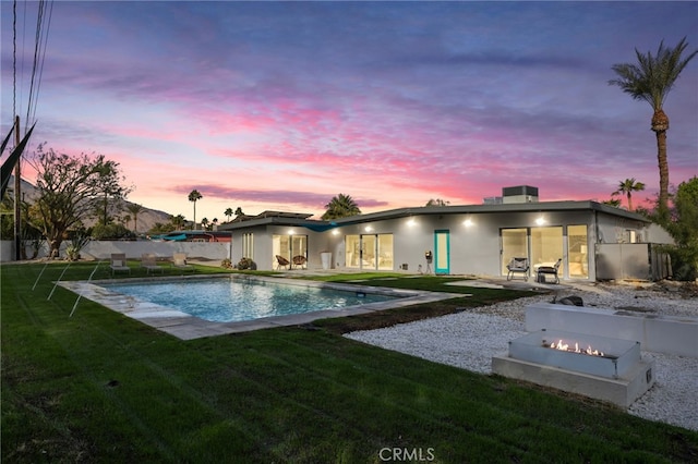 pool at dusk featuring a lawn, a patio area, and a fire pit