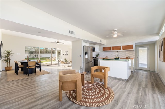 kitchen with ceiling fan, backsplash, appliances with stainless steel finishes, and light hardwood / wood-style floors