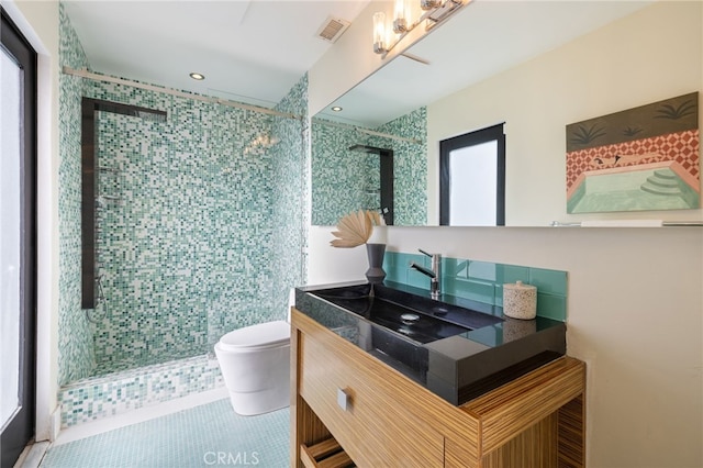 bathroom with toilet, vanity, tile patterned floors, and a tile shower