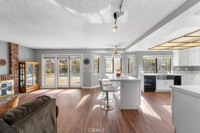 kitchen featuring ceiling fan, a center island, black dishwasher, a kitchen breakfast bar, and white cabinets