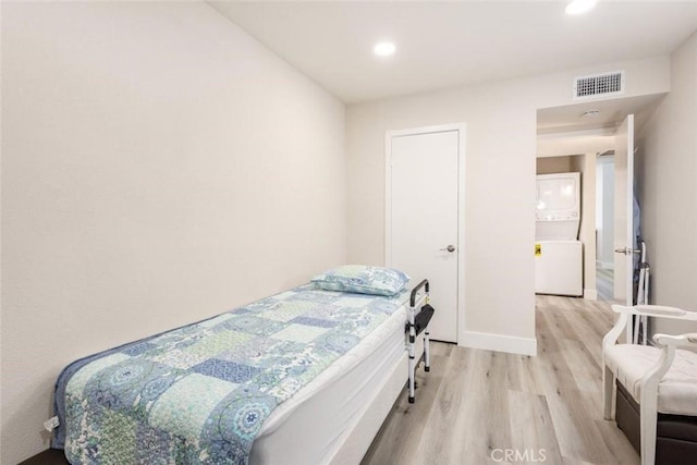 bedroom with stacked washer / dryer and light wood-type flooring