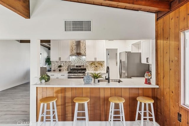 kitchen with a kitchen breakfast bar, white cabinetry, wall chimney range hood, and appliances with stainless steel finishes