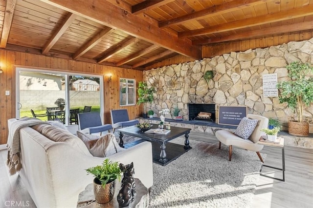 living room featuring wooden ceiling, a stone fireplace, vaulted ceiling with beams, wood walls, and light wood-type flooring