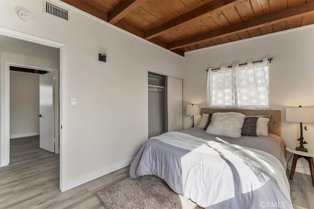 bedroom with beam ceiling, light wood-type flooring, a closet, and wooden ceiling