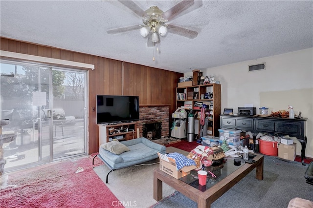 carpeted living room with wooden walls, a fireplace, ceiling fan, and a textured ceiling