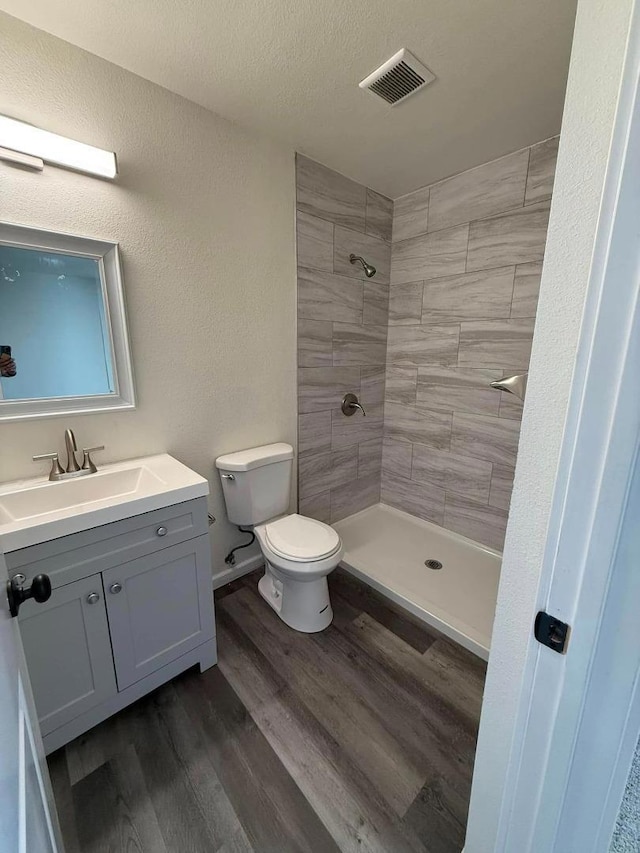 bathroom featuring hardwood / wood-style floors, a textured ceiling, vanity, toilet, and a tile shower