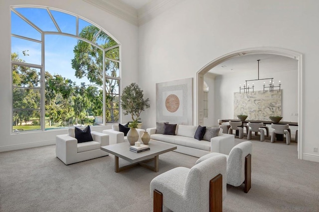 carpeted living room with a towering ceiling, ornamental molding, and a notable chandelier