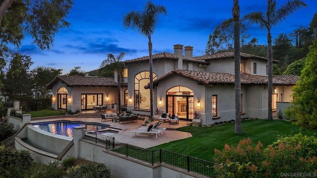 back house at dusk with a lawn, outdoor lounge area, and a patio