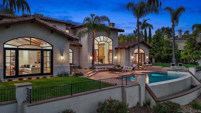 back house at dusk featuring a yard, an outdoor living space, a fenced in pool, and a patio area