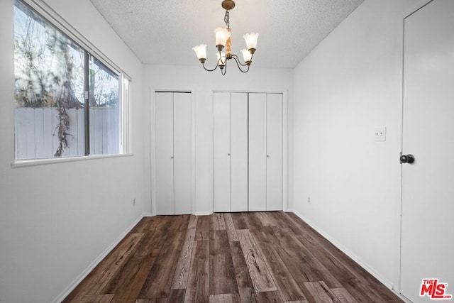 unfurnished bedroom with a notable chandelier, dark hardwood / wood-style floors, a textured ceiling, and two closets