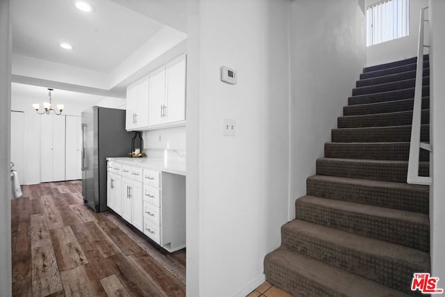 stairs with hardwood / wood-style flooring, a raised ceiling, and a notable chandelier