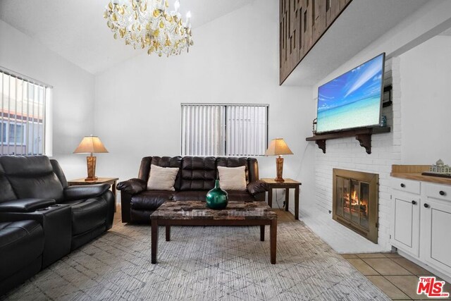 living room featuring a notable chandelier, high vaulted ceiling, a brick fireplace, and light tile patterned floors