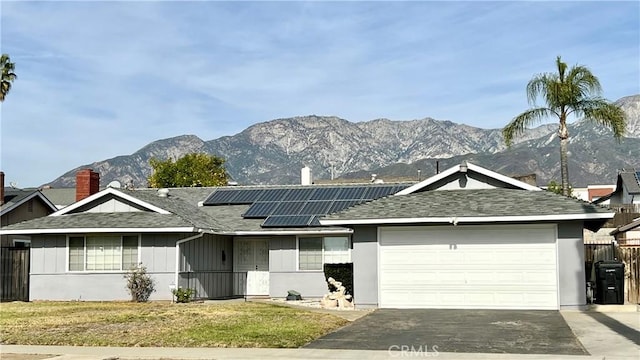 single story home featuring a mountain view, a front yard, solar panels, and a garage