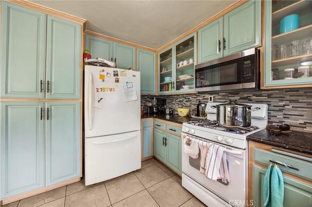 kitchen featuring dark stone countertops, white appliances, light tile patterned floors, and tasteful backsplash