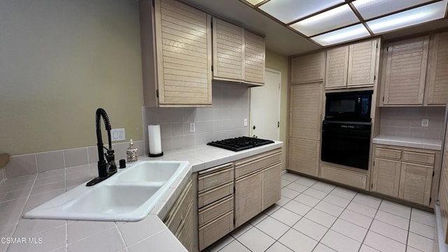 kitchen featuring backsplash, black appliances, sink, light tile patterned floors, and tile counters