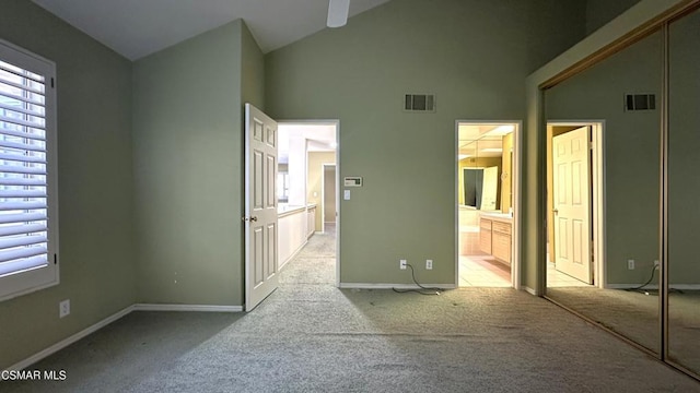 unfurnished bedroom with light carpet, ensuite bathroom, and high vaulted ceiling