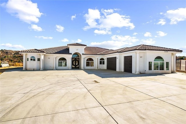 mediterranean / spanish house featuring an attached garage, a tiled roof, stucco siding, and driveway