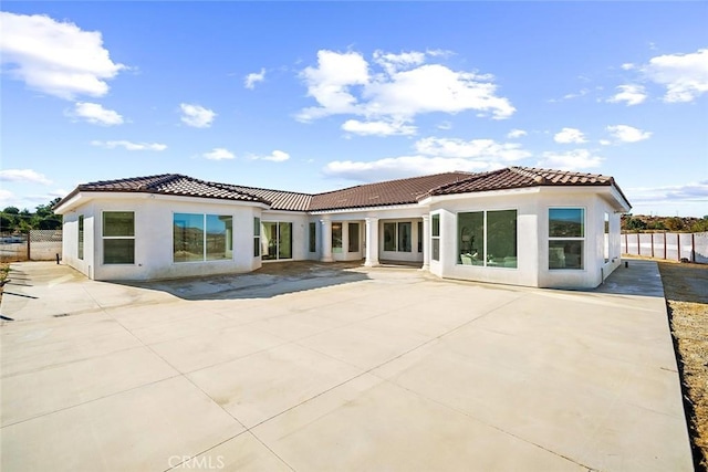 rear view of house with fence, a tiled roof, and stucco siding