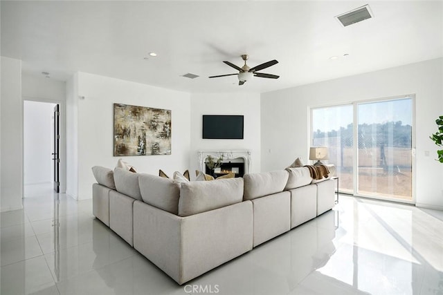 living area featuring a ceiling fan, a glass covered fireplace, visible vents, and light tile patterned floors