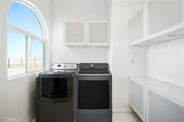 clothes washing area with baseboards, washer and dryer, and cabinet space