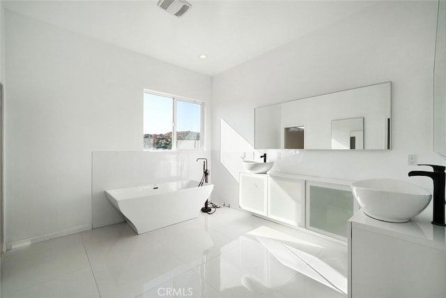 bathroom with double vanity, visible vents, tile patterned flooring, a freestanding tub, and a sink