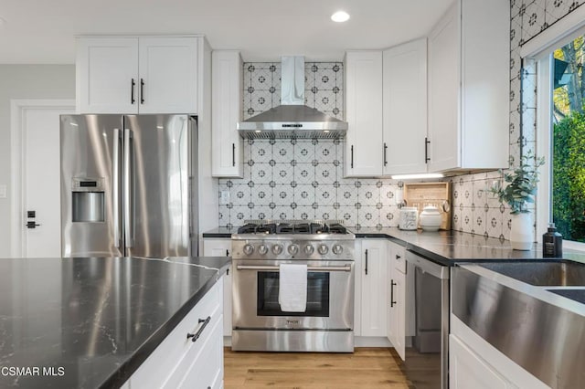 kitchen featuring white cabinetry, light hardwood / wood-style floors, stainless steel appliances, backsplash, and wall chimney range hood