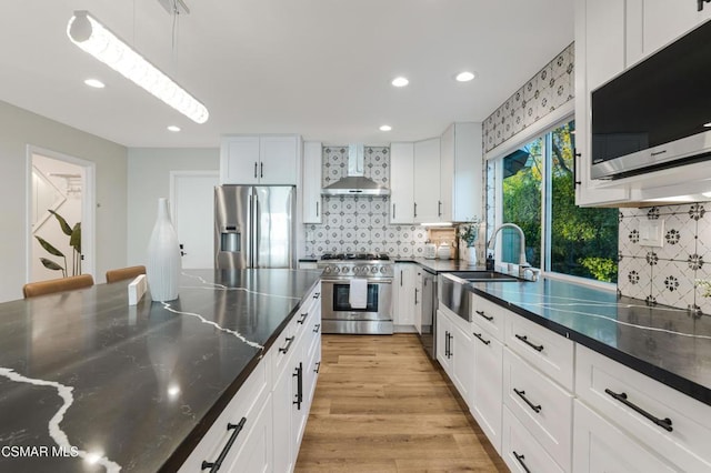 kitchen with pendant lighting, sink, white cabinetry, appliances with stainless steel finishes, and wall chimney exhaust hood