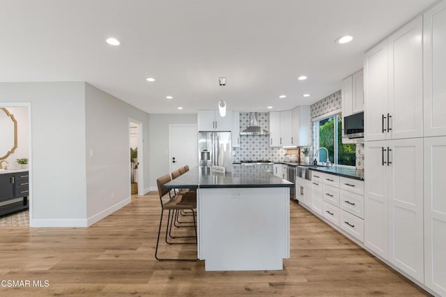 kitchen with white cabinets, wall chimney exhaust hood, a kitchen island, decorative light fixtures, and stainless steel appliances