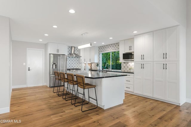 kitchen featuring white cabinets, appliances with stainless steel finishes, wall chimney exhaust hood, and a kitchen island