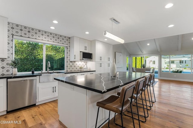 kitchen with a kitchen island, vaulted ceiling with beams, hanging light fixtures, appliances with stainless steel finishes, and white cabinets