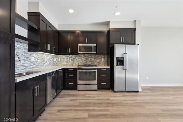 kitchen featuring appliances with stainless steel finishes, backsplash, light wood-type flooring, dark brown cabinetry, and sink