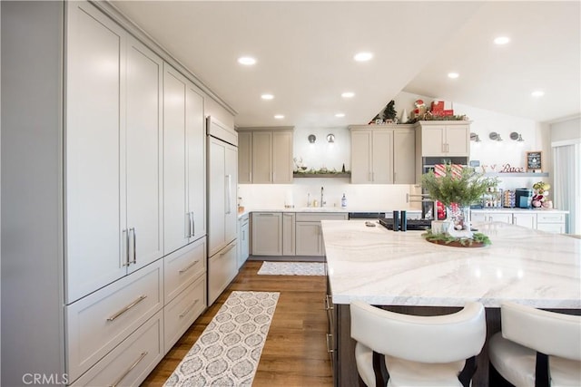 kitchen featuring a kitchen breakfast bar, light stone counters, dark wood-type flooring, paneled built in fridge, and lofted ceiling