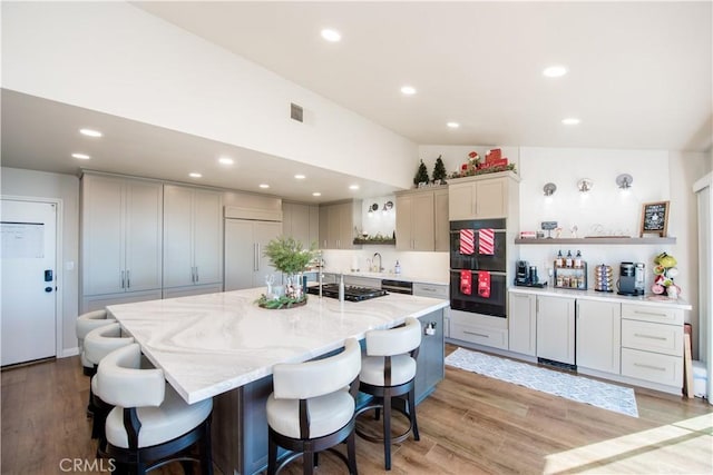 kitchen featuring a large island with sink, black appliances, lofted ceiling, and light wood-type flooring