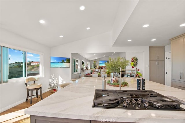 kitchen featuring lofted ceiling, a kitchen breakfast bar, light hardwood / wood-style flooring, light stone countertops, and stainless steel gas cooktop