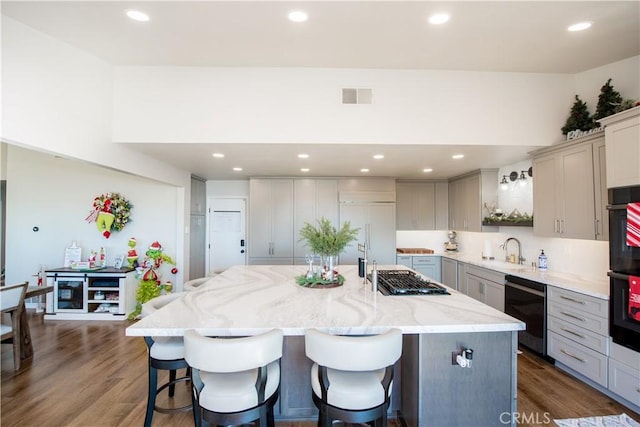 kitchen with sink, dark wood-type flooring, light stone counters, an island with sink, and gray cabinets