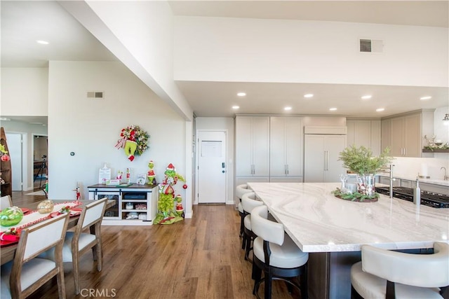 kitchen with paneled fridge, a kitchen breakfast bar, light stone counters, a towering ceiling, and wood-type flooring