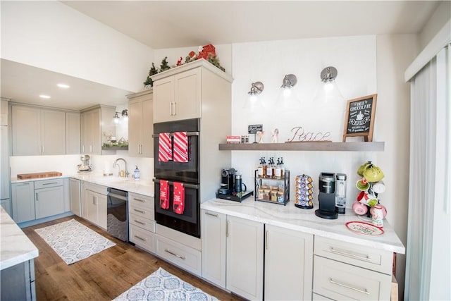 kitchen featuring sink, black double oven, stainless steel dishwasher, dark hardwood / wood-style floors, and light stone counters