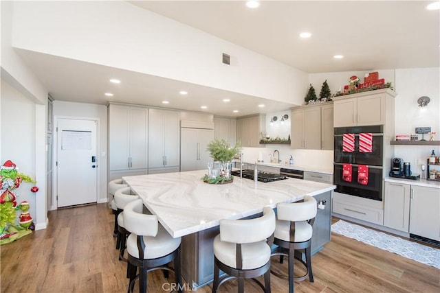 kitchen with light stone countertops, appliances with stainless steel finishes, a kitchen breakfast bar, a kitchen island with sink, and light hardwood / wood-style flooring